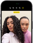 iPhone 18 Pro nero mostrato di fronte, sul display due persone in posa davanti alla fotocamera frontale Center Stage