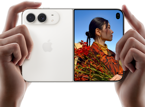 Due mani tengono un iPhone Duo bianco stellare in orizzontale, aperto; sul pannello sinistro si nota la doppia fotocamera posteriore Fusion da 48MP, mentre sul pannello destro si vede una persona che si fa fotografare sullo schermo esterno; il soggetto può vedere il proprio volto mentre viene scattata la foto grazie alla funzione Duo Preview